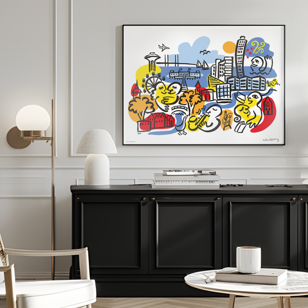 A colorful framed art print featuring cartoon-style cityscape illustrations hangs on a light gray wall in a modern living room setting with a wooden armchair, black sideboard, and white lamps.