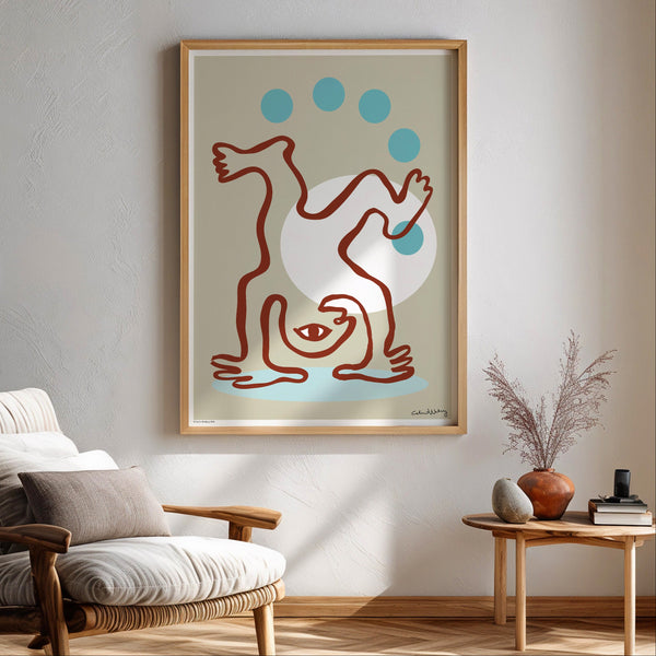 A framed abstract art print hangs on a light gray wall in a styled living room corner with a wooden armchair, side table, plants, and warm sunlight.