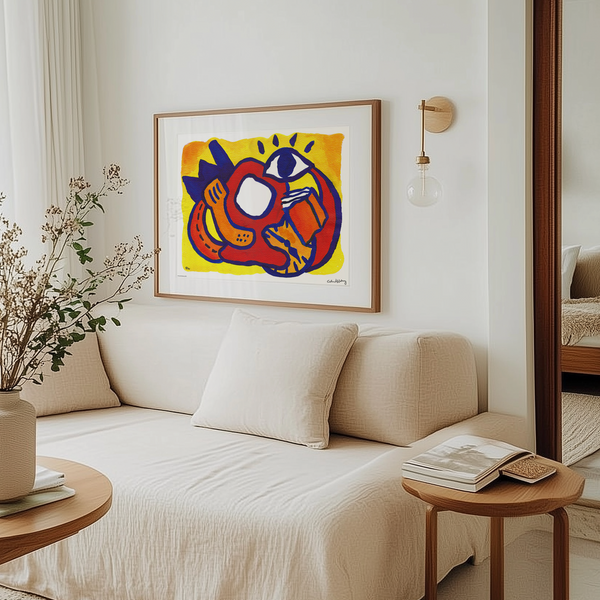 


A framed abstract art print featuring a stylized red, orange, and blue cat on a yellow background, displayed on a white wall above a cream-colored sofa in a modern, sunlit living room.